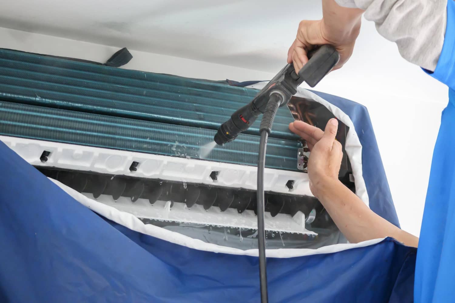 Technician pressure-washing an indoor air conditioner coil