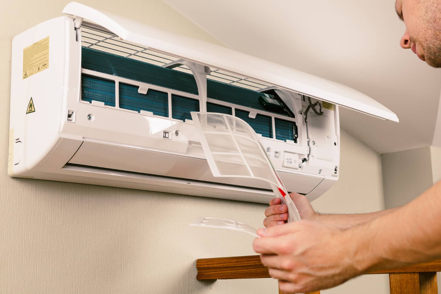 Man removing filter from wall-mounted air conditioner