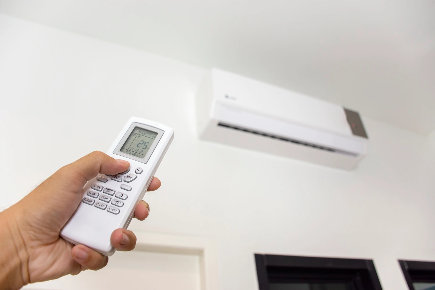 Hand holding air conditioner remote towards wall unit